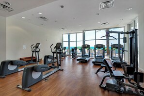 Ein großzügiger Fitnessraum mit verschiedenen Cardiogeräten, Kraftstationen und einem großen Fenster mit Blick ins Freie.