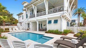 Una casa de dos pisos con piscina, mobiliario exterior y un porche cubierto.