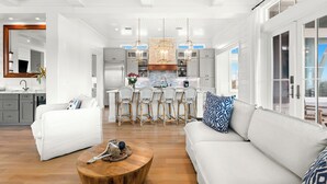 Una cocina moderna con una isla central, armarios blancos y un comedor con sillas de mimbre.