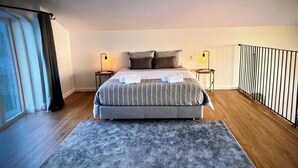 Een slaapkamer met een groot bed, twee nachtkastjes met lampen, een grijs vloerkleed en een raam met gordijnen.