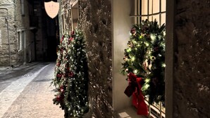 Una estrecha calle adoquinada con un edificio de ladrillo a la izquierda y una ventana decorada con un árbol de Navidad a la derecha.