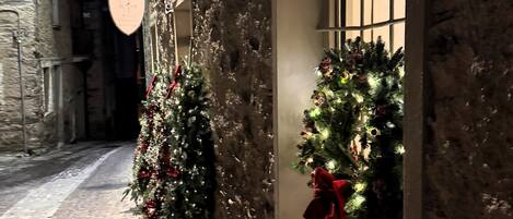 A narrow cobblestone street with a brick building on the left and a window with a Christmas tree on the right.