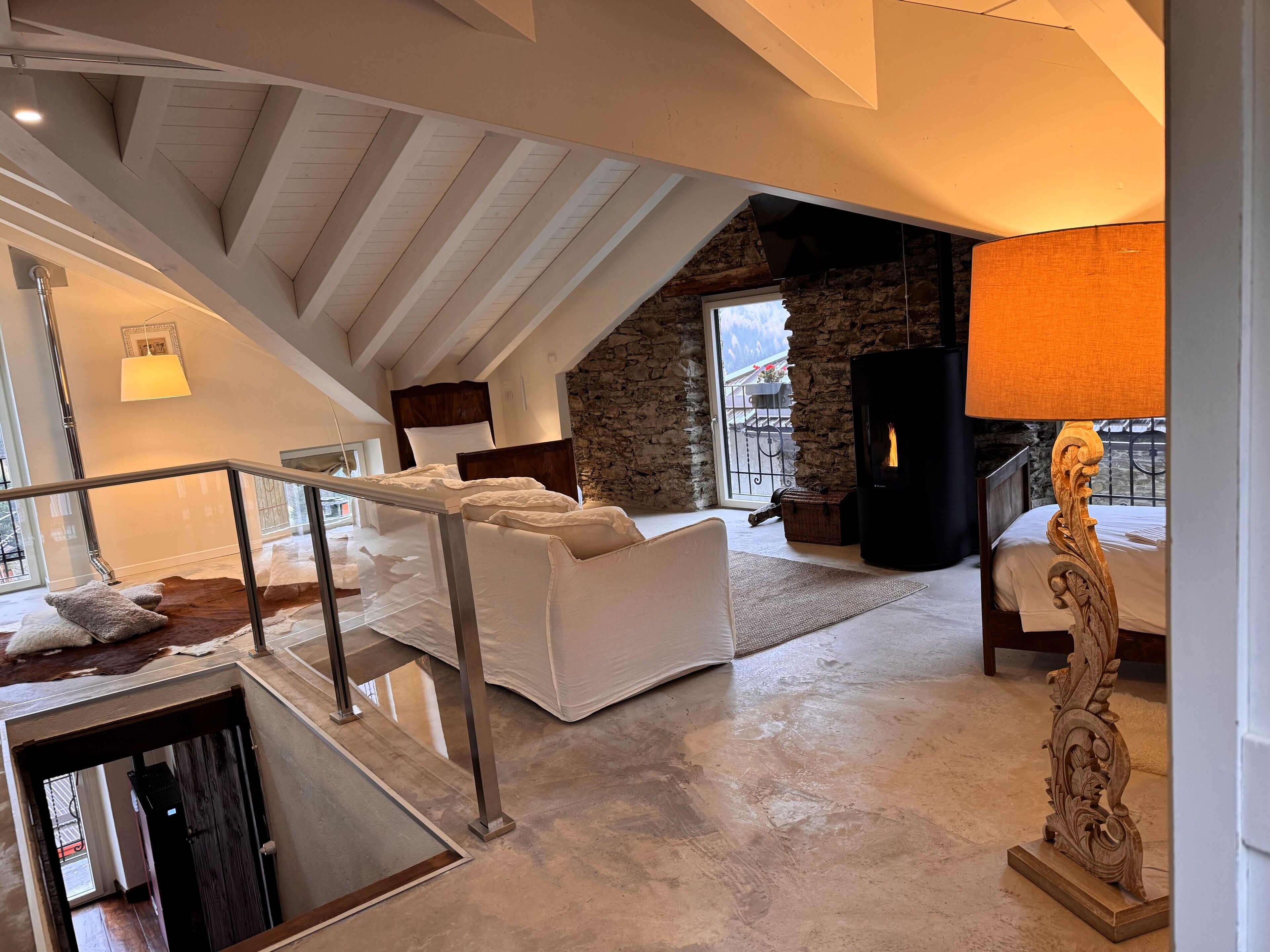 Amplio dormitorio tipo loft con pared de piedra, chimenea y ventana grande que da a un balcón.