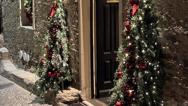 Un edificio con fachada de piedra, una puerta negra y dos árboles de Navidad decorados con adornos rojos.