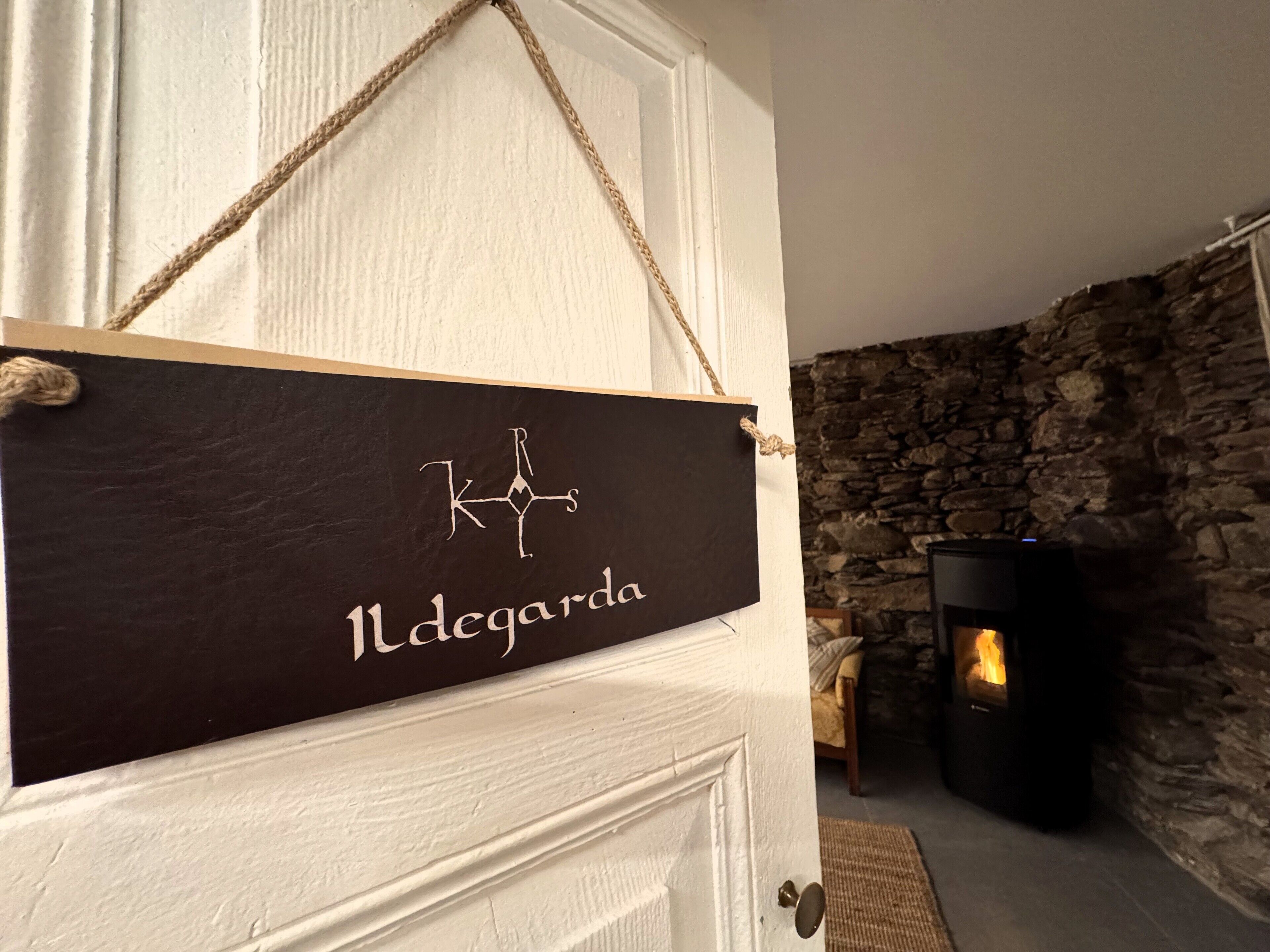 Ein Schild mit dem Text "1 degarda" an einer Tür, eine Steinsäule und ein Kaminofen im Hintergrund.
