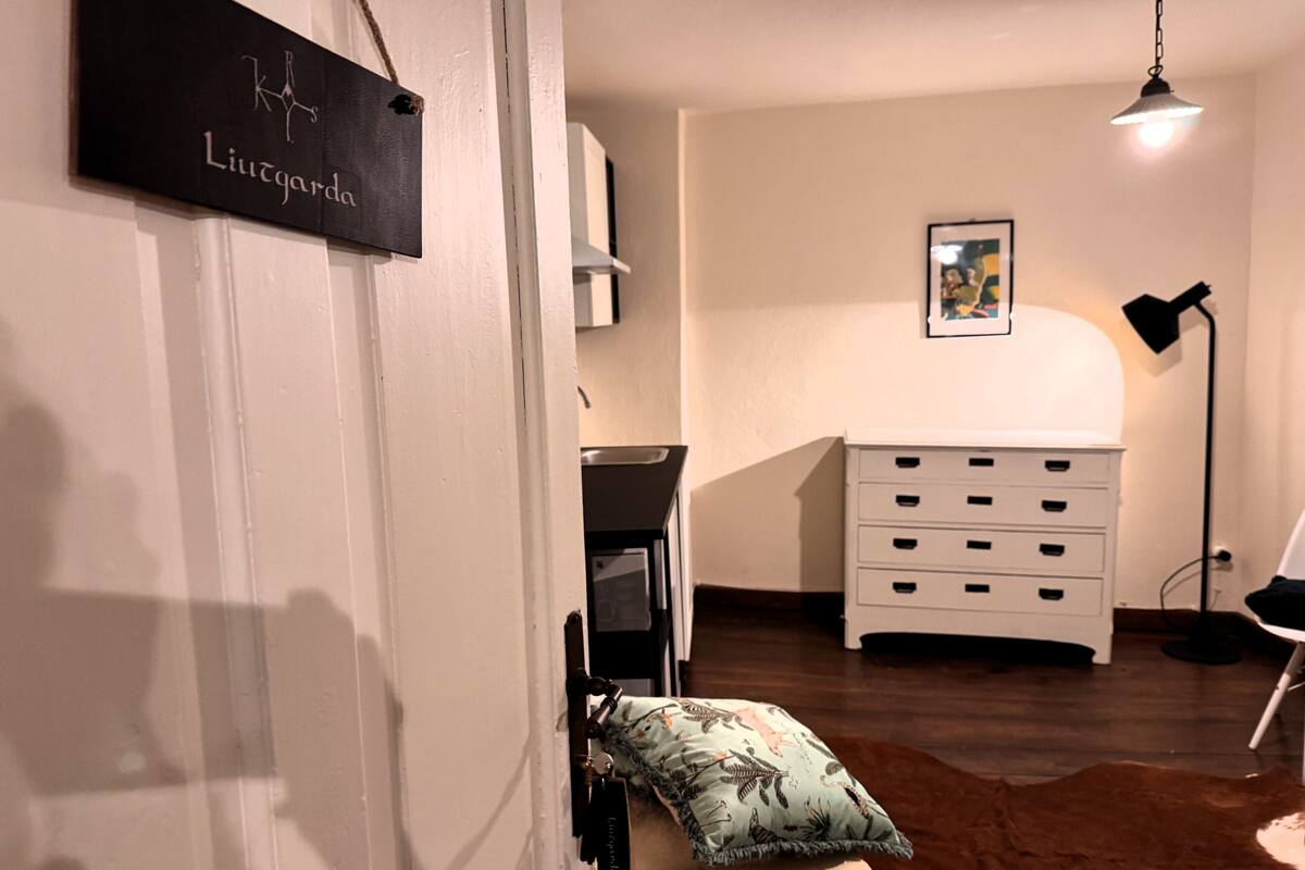 A room with a white dresser, a hanging light fixture, and a door with a sign.