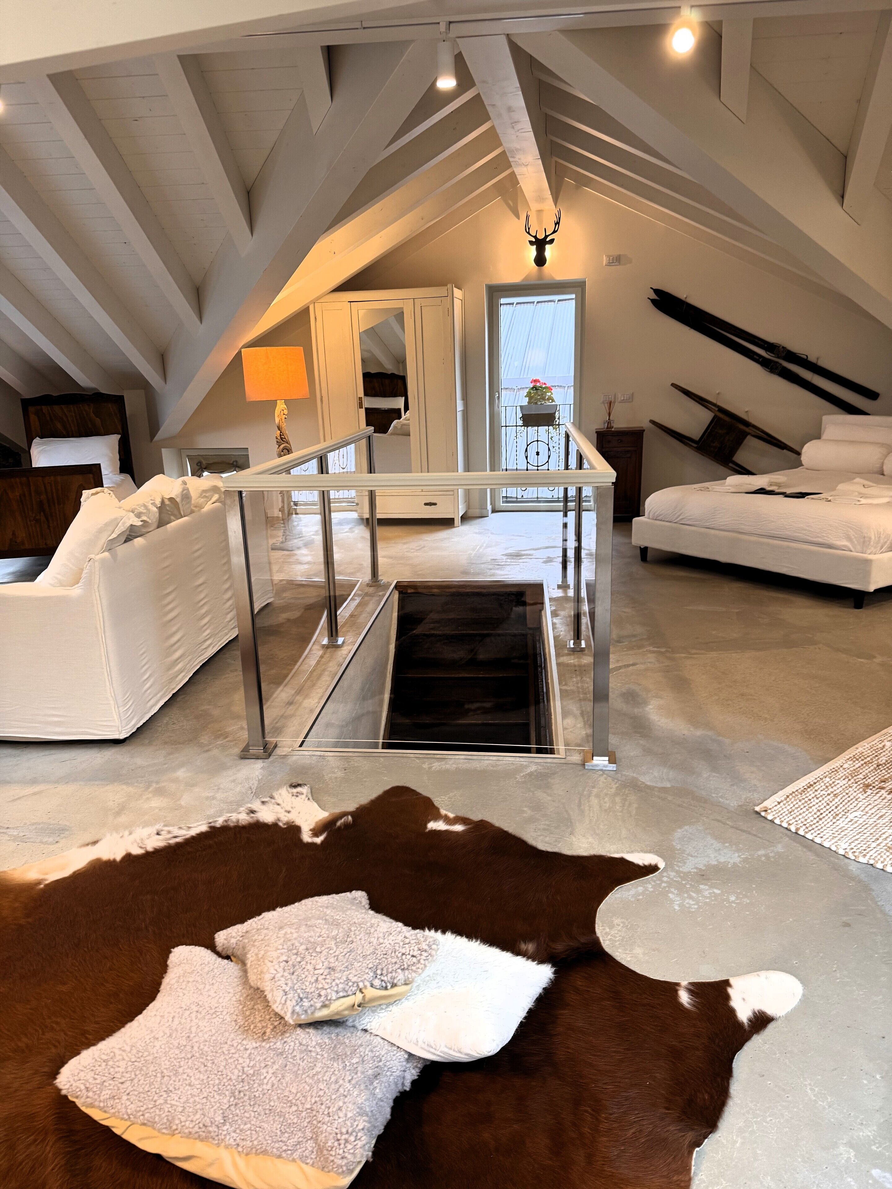 An attic bedroom with a high ceiling, a bed, a white sofa, a glass door leading to a balcony, and a cowhide rug.