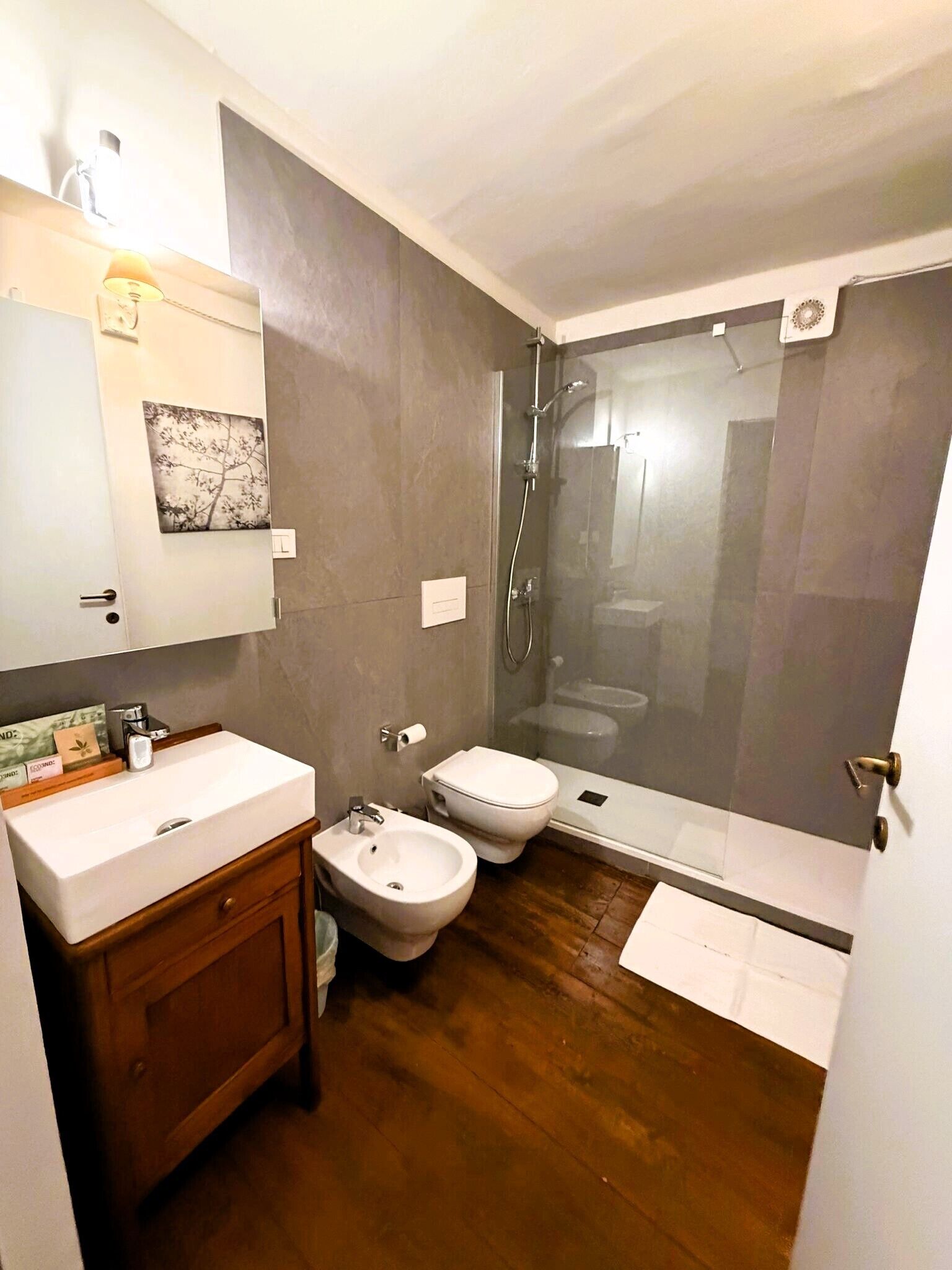 Ein modernes Badezimmer mit einem Holzwaschtisch, einem Bidet, einer Toilette und einer Duschkabine.