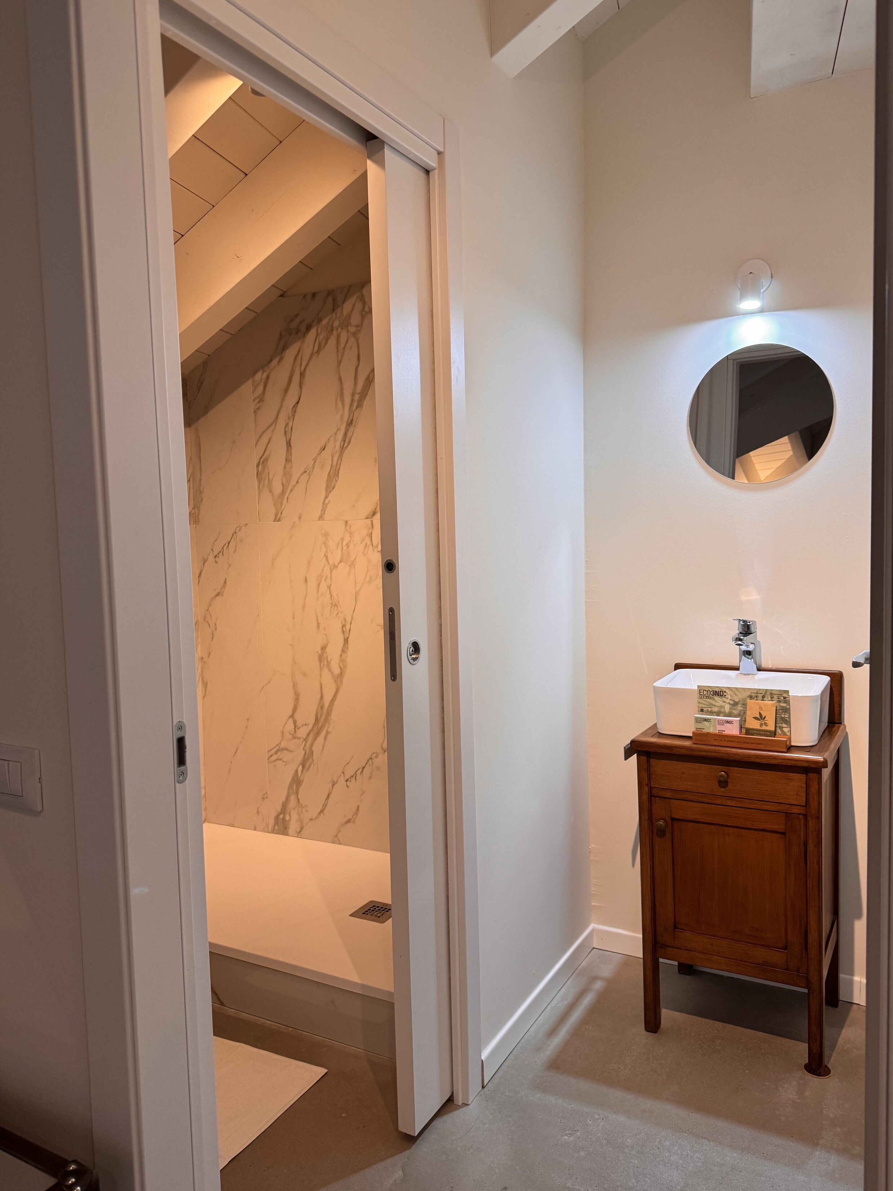 Un baño con pared de mármol, un lavamanos con espejo y un mueble de madera.