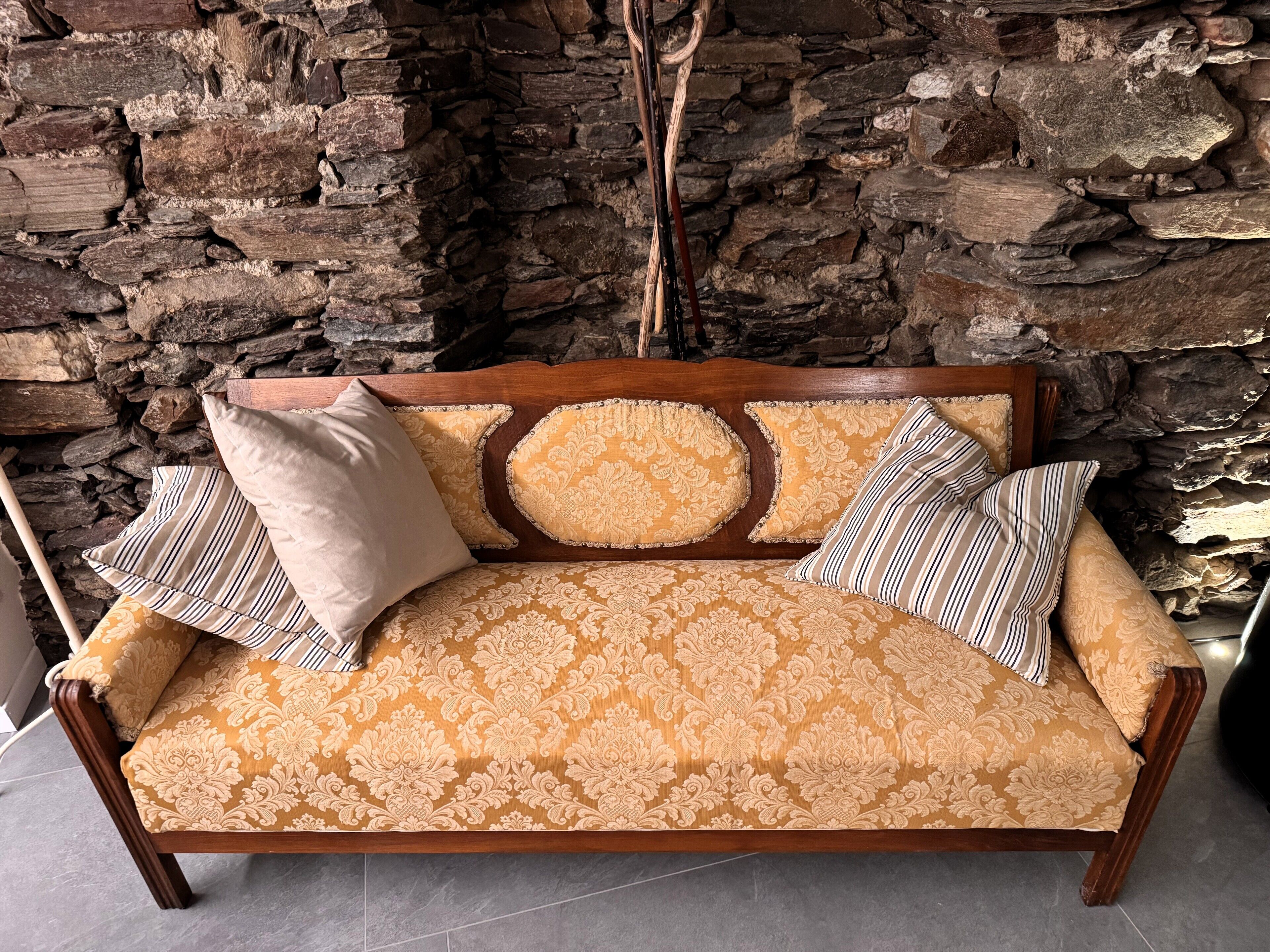 Ein Holzsofa mit einem gemusterten Kissen vor einer Steinwand.