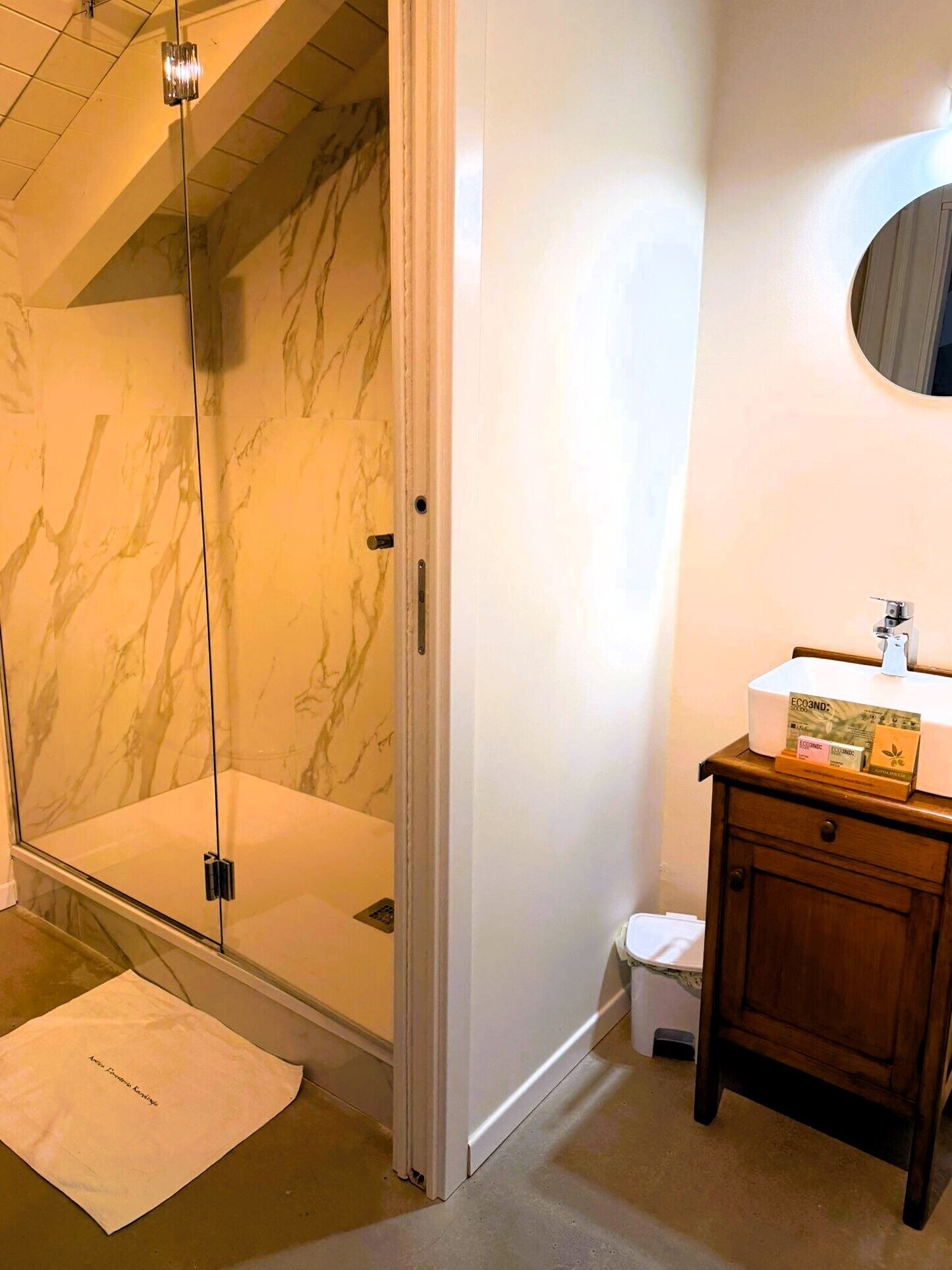 A bathroom with a glass-enclosed shower, a white sink with a mirror, and a wooden cabinet.