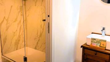 A bathroom with a glass-enclosed shower, a white sink with a mirror, and a wooden cabinet.