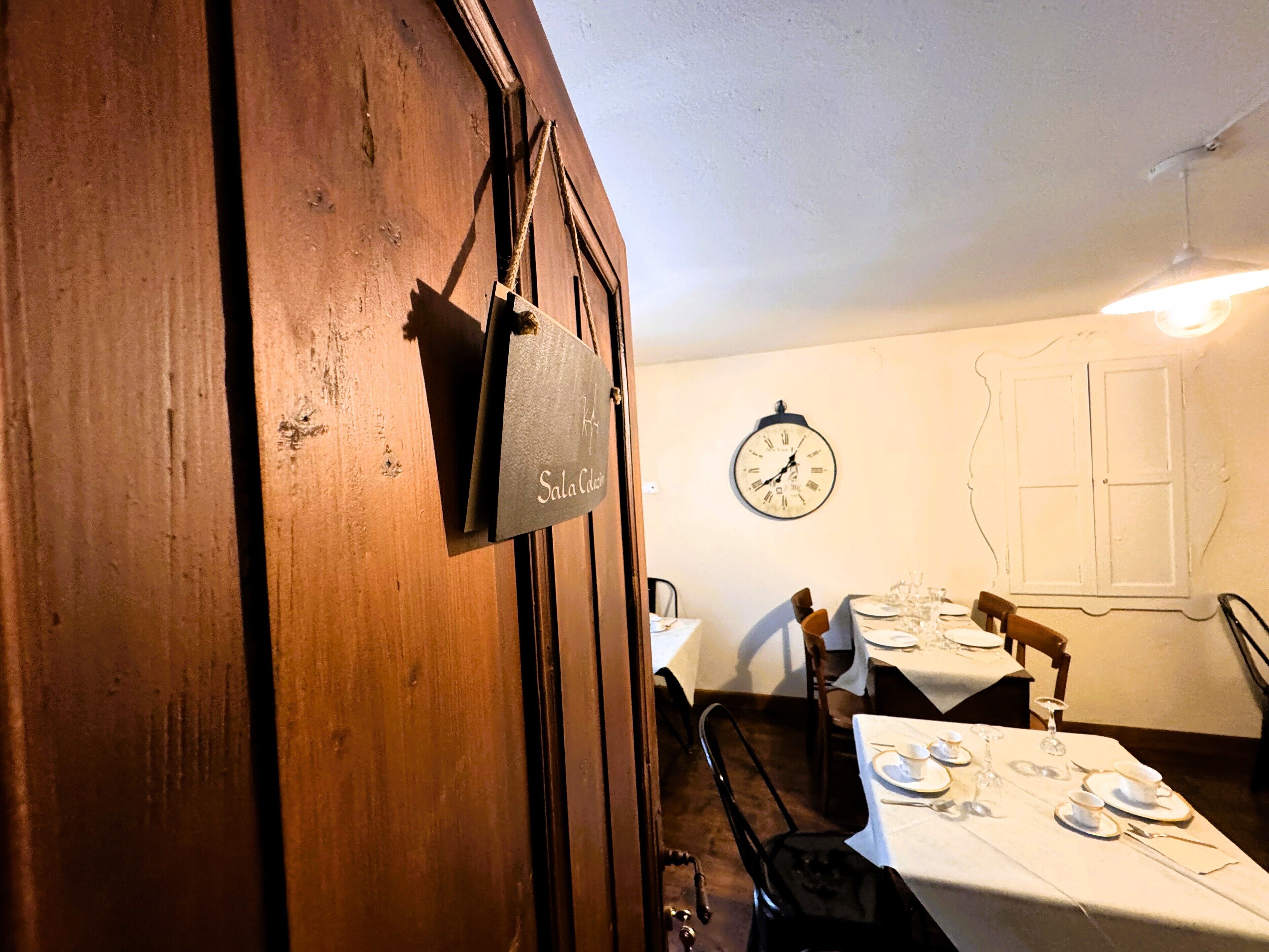 A dining area with a wooden door, a clock on the wall, and tables set for dining.