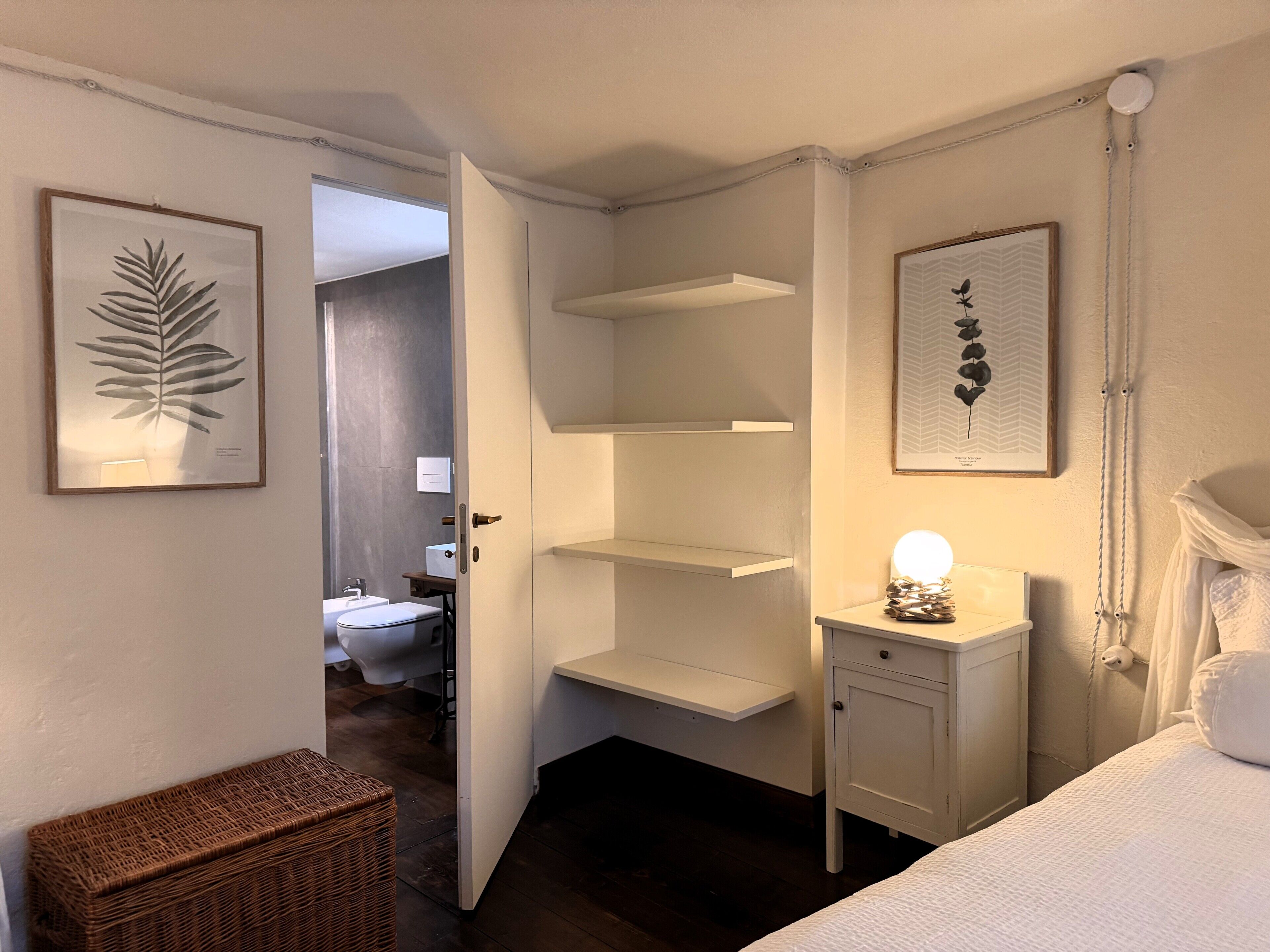 Ein Schlafzimmer mit einem Bett, einem Nachttisch mit Lampe, einem Kleiderschrank und einer Tür zu einem Badezimmer.