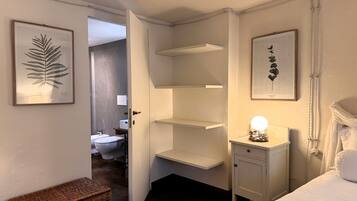 Ein Schlafzimmer mit einem Bett, einem Nachttisch mit Lampe, einem Kleiderschrank und einer Tür zu einem Badezimmer.