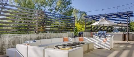 Un patio exterior con un sofá blanco modular, una chimenea y una pérgola con luces colgantes.