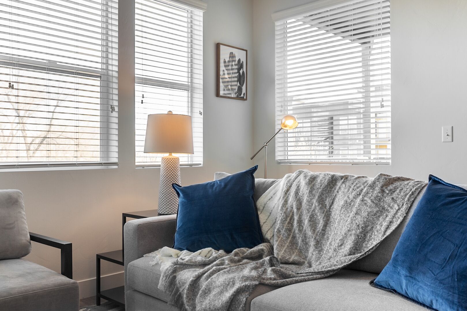 A cozy living room with a grey sofa, blue cushions, a patterned throw blanket, and a floor lamp.