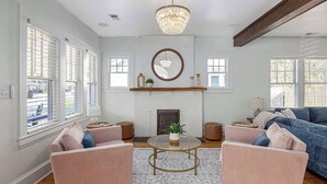 Un salon spacieux avec une cheminée, deux fauteuils roses, un canapé bleu et un lustre.