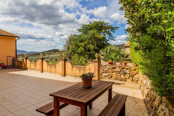 A patio with a wooden table and benches, surrounded by stone walls and potted plants.