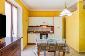 A compact kitchen with white cabinets, a tiled backsplash, and a dining area with a patterned tablecloth.