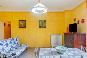 A room with a sofa, a dining table, a television, and artwork on the walls.