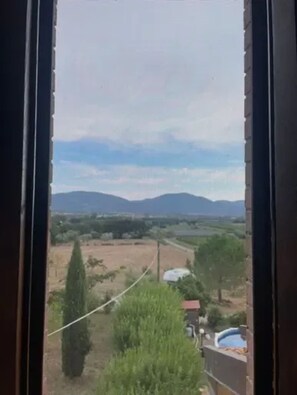 Blick durch ein Fenster auf eine Landschaft mit Feldern, Bäumen und fernen Bergen.