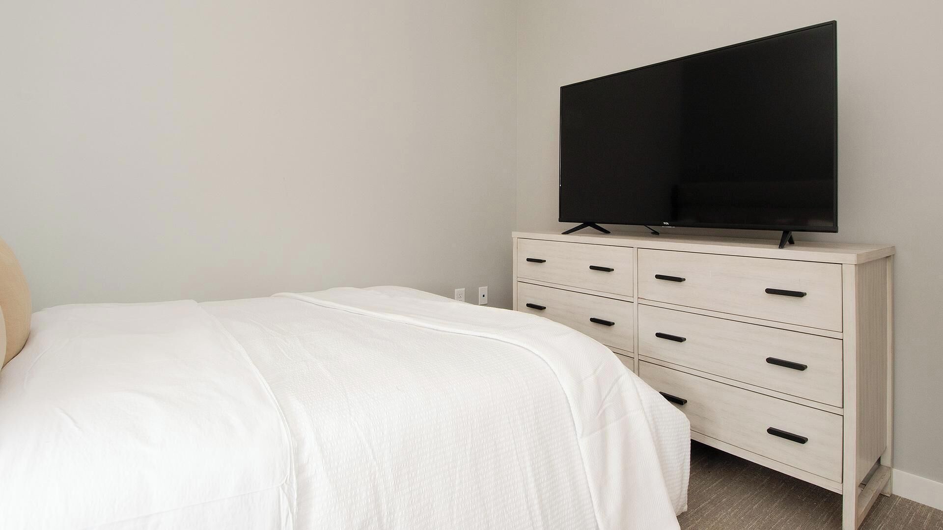 Un dormitorio con cama, cómoda con cajones y televisor de pantalla plana montado sobre la cómoda.
