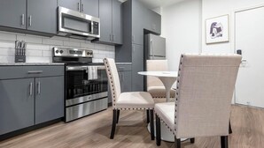 A modern kitchen with grey cabinets, a built-in oven, microwave, and refrigerator. There is a dining table with two chairs. - Landing | Amazing 1BD, Courtyard, Clubhouse (St. Louis)