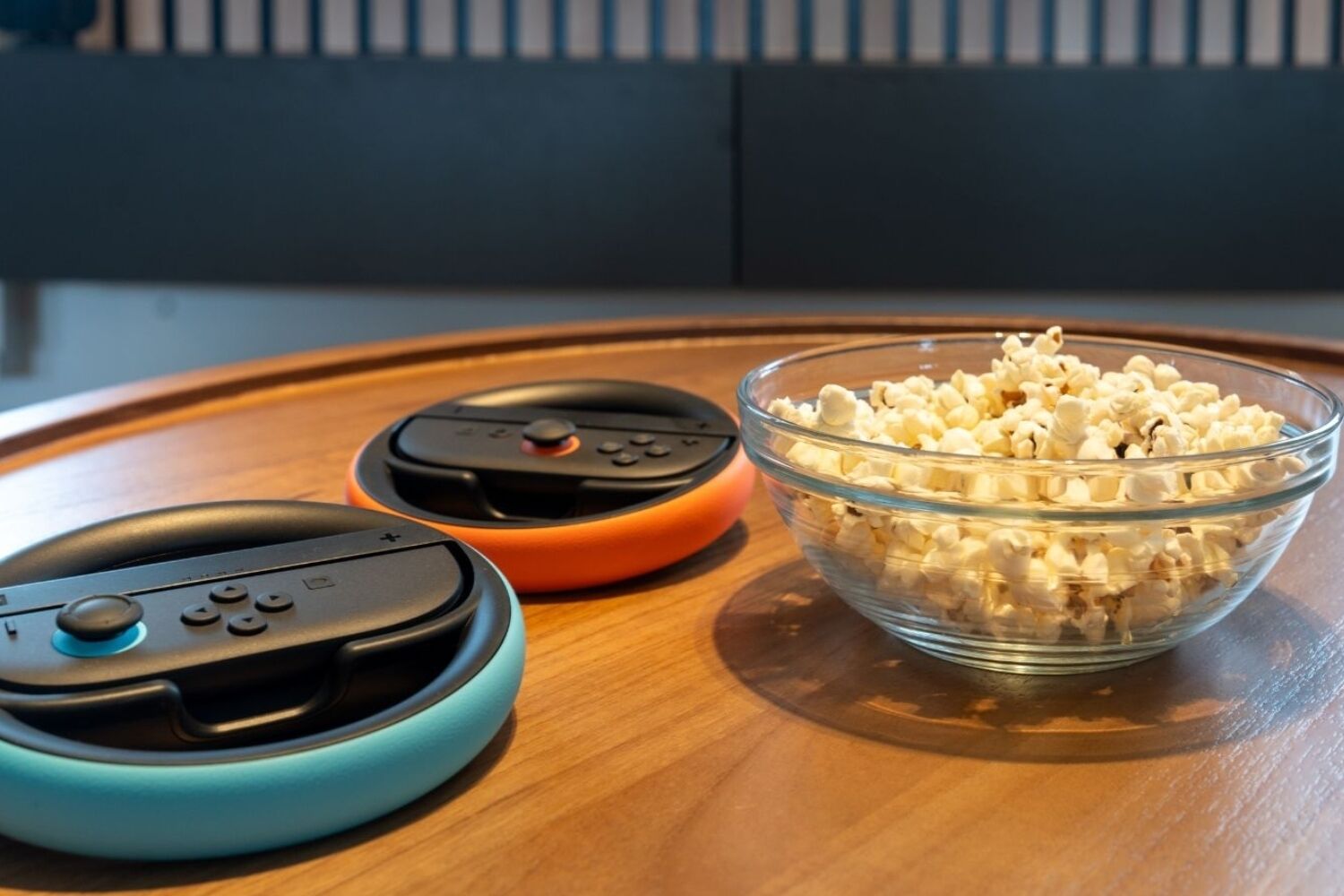 A wooden table with two gaming controllers and a bowl of popcorn.