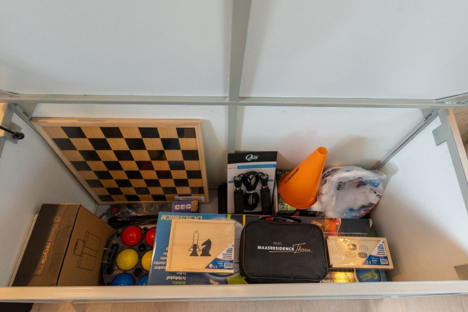 Ein Lagerraum mit Schachbrettmuster, einer schwarzen Tasche, einem blauen Karton und diversen Gegenständen, darunter ein Tennisschläger.