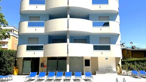 Ein mehrstöckiges Hotel mit Poolbereich, das einen modernen architektonischen Stil mit Balkonen und blauem Himmel aufweist.