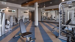 Ett gym med olika typer av träningsutrustning, inklusive en bänkpress, styrketräningsmaskiner och lösa vikter.