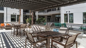 An outdoor patio with a grill area, seating, and a view of the building's exterior. - Landing | Amazing 2BD, Gym, Pool (Jacksonville)