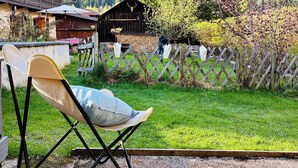 A rustic wooden cabin with a mountain backdrop, a lawn chair, and a wooden fence.