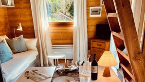 A cozy cabin interior with a dining table set, a sofa, a small table, and a ladder.