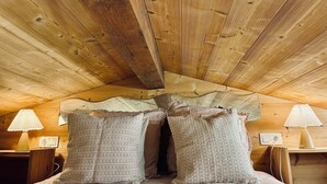 A wooden ceiling with a sloped design, a bed with patterned pillows, and bedside lamps.