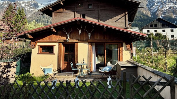 A wooden chalet with a balcony, a dining area, and a view of snow-capped mountains.