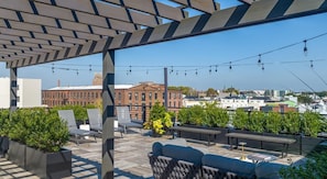 A rooftop terrace with outdoor seating, a pergola, and a view of a cityscape. - Landing | Spectacular 1BD, Rooftop Lounge (Philadelphia)