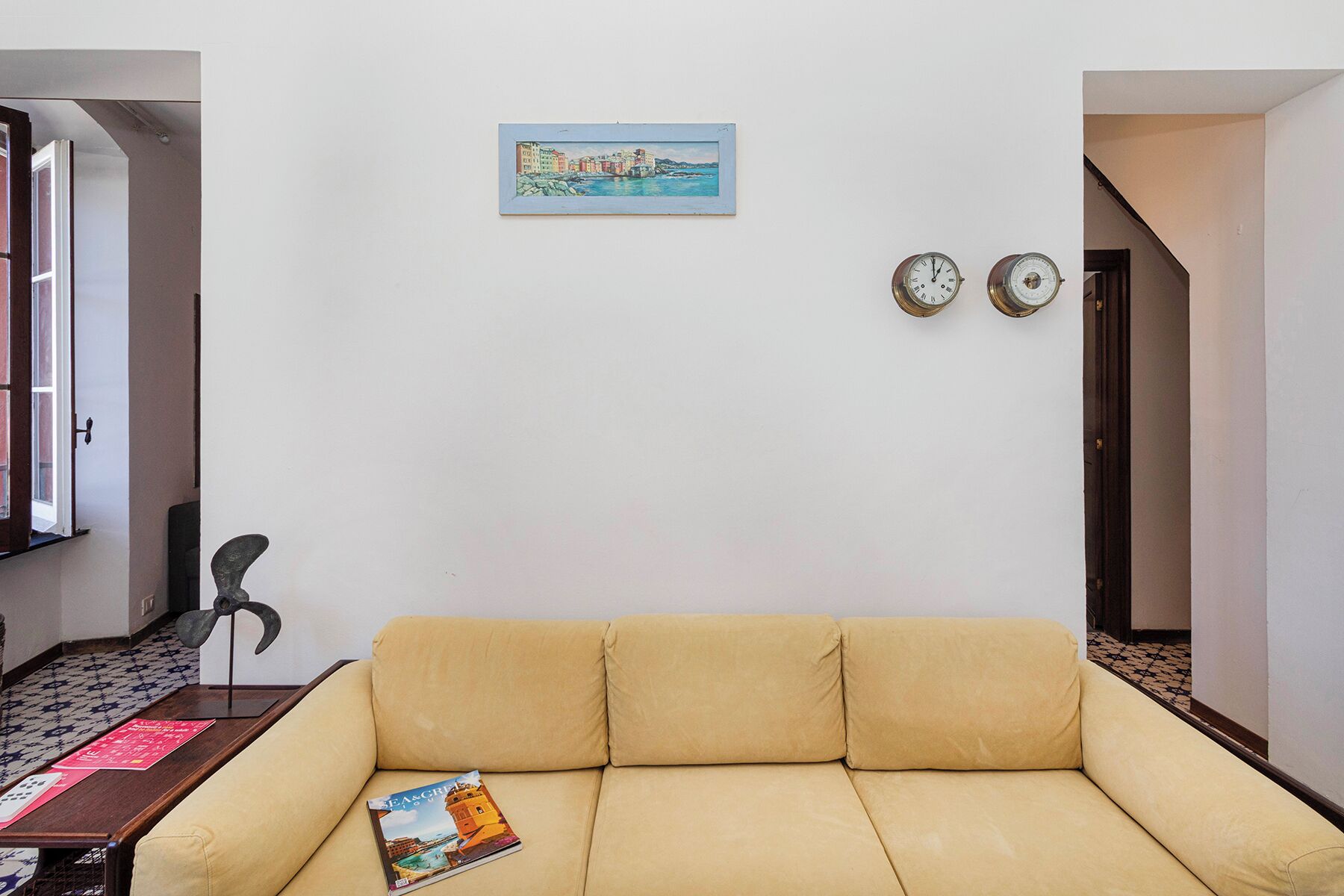 A living room with a beige sofa, a framed painting, and two wall clocks.