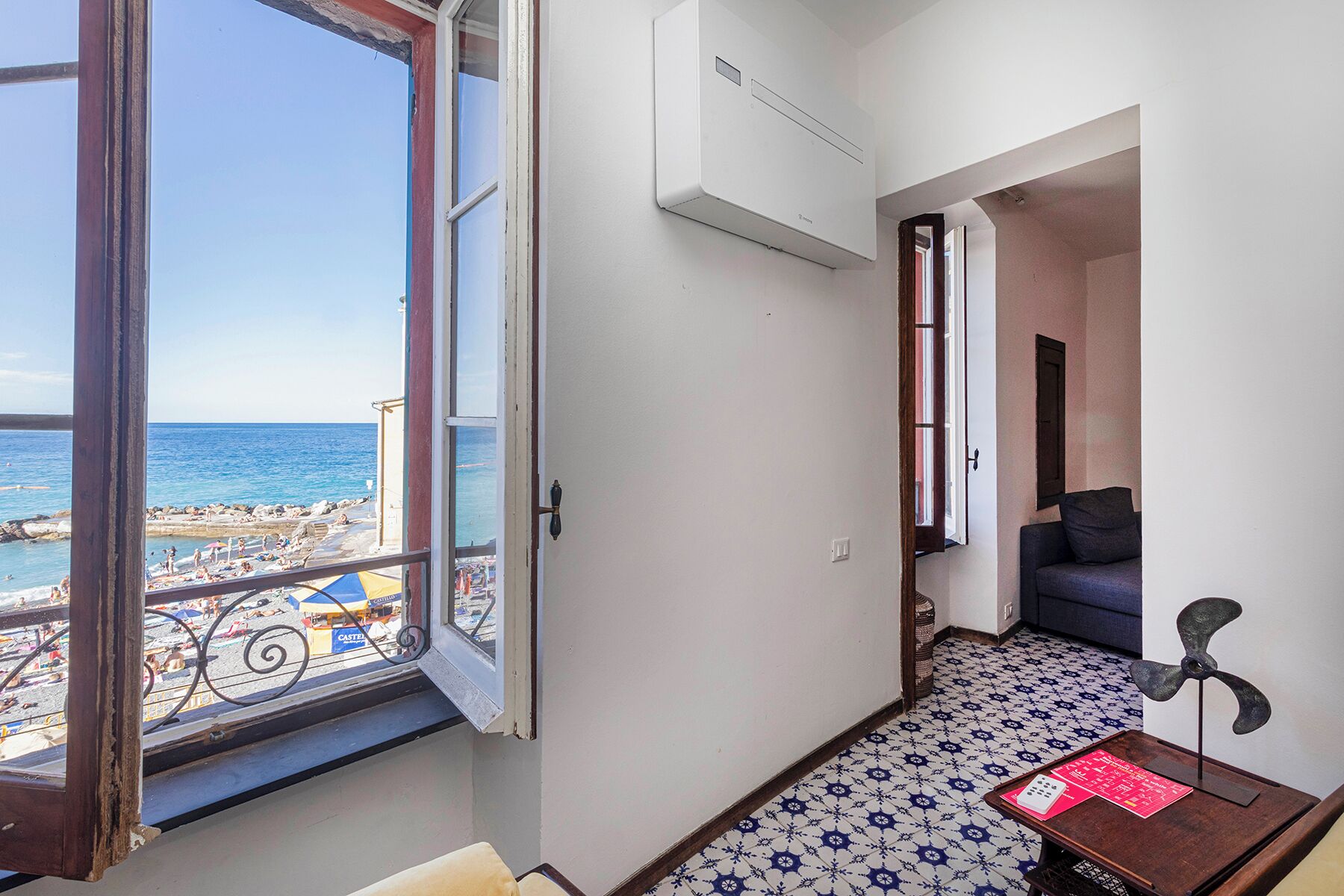 A hotel room with a view of the beach, a small table with a lamp, and a tiled floor.
