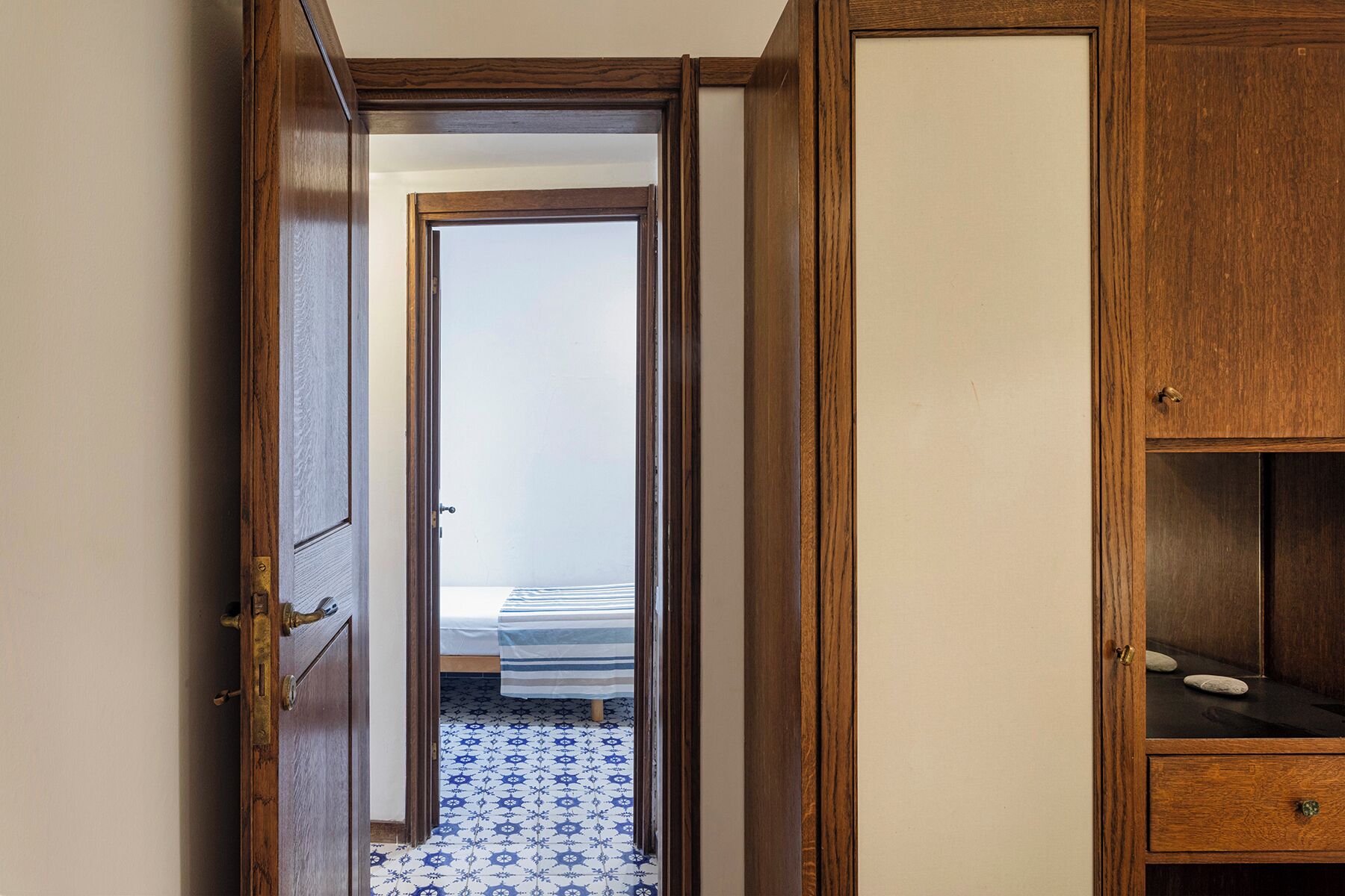 Un pasillo estrecho con una puerta de madera que da a un dormitorio con cama y suelo estampado.