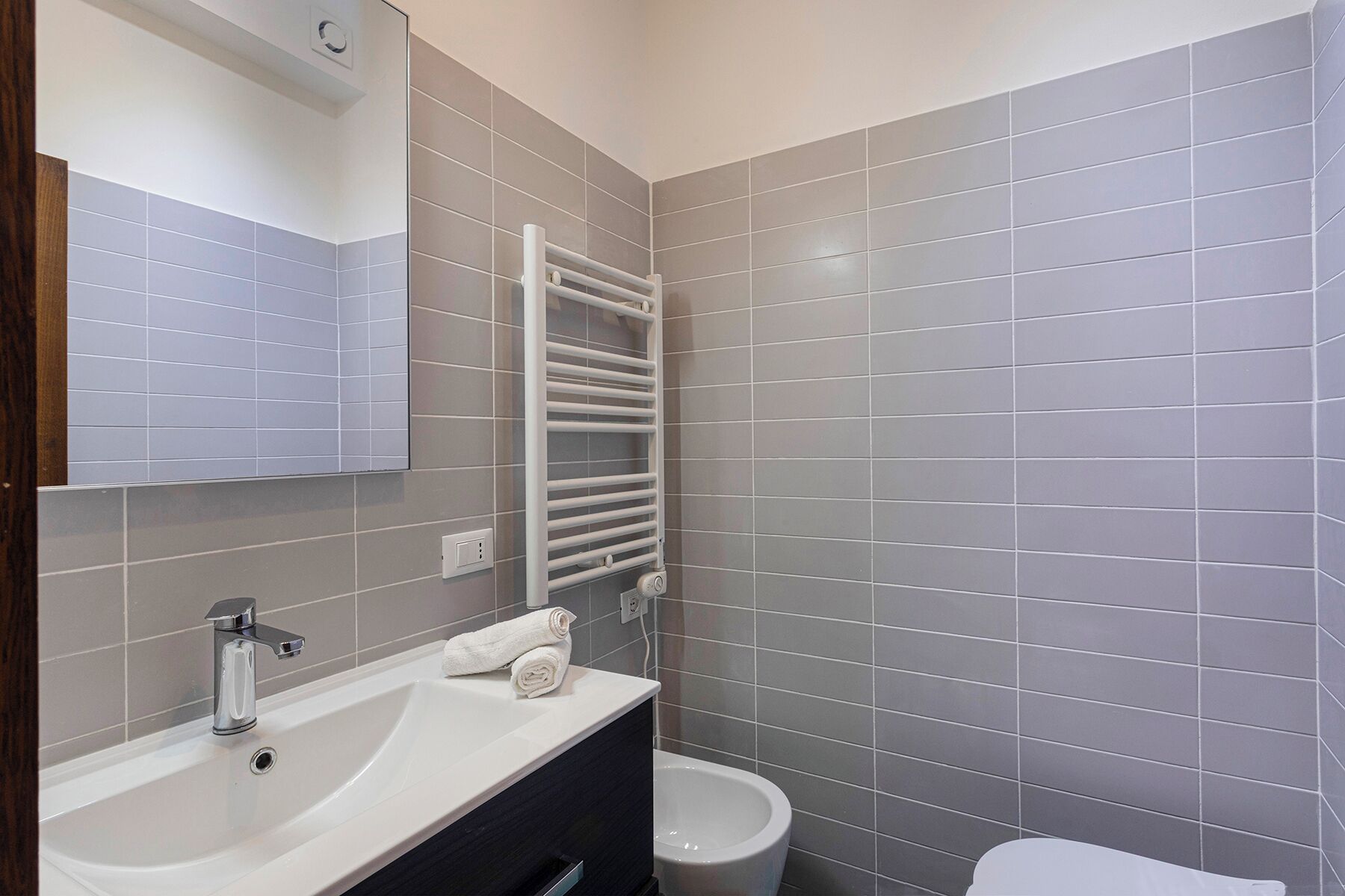 A modern bathroom with a white sink, a towel, a toilet, and a towel rack.