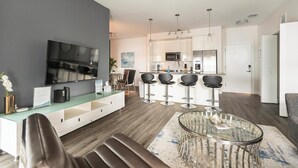 Ein modernes Wohnzimmer mit einem Glastisch, einem Fernseher und einer Sitzecke mit einer Couch und Sesseln.