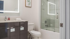 Ein modernes Badezimmer mit einer Duschkabine, einer weißen Toilette und einem Waschtisch mit Spiegel.