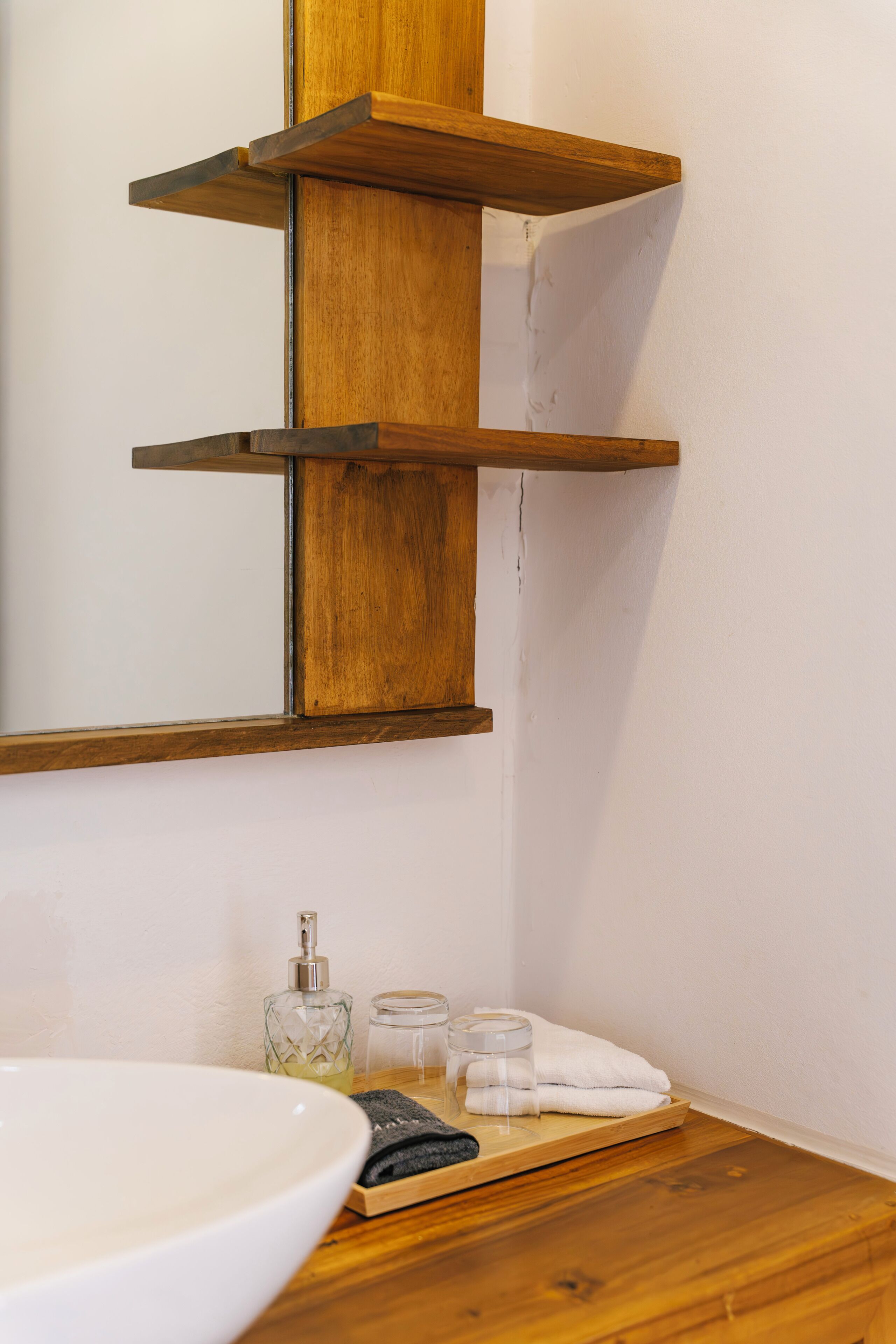 Ein Badezimmer mit Holzregal, Waschbecken, einer Seifenspender aus Glas und einem Handtuchhalter.