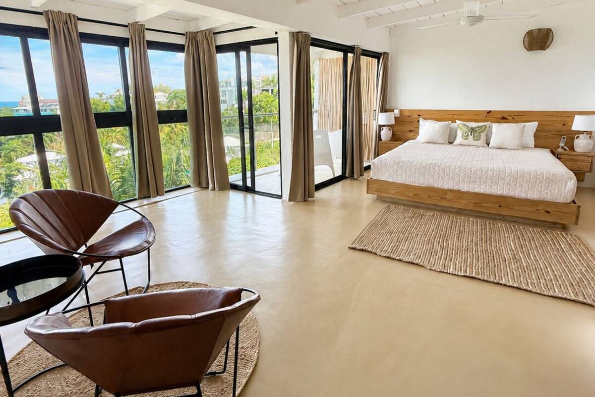 A spacious bedroom with a large bed, a view of the outdoors, and a dining area with chairs.