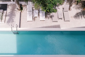 Ein Luftbild eines Schwimmbeckens mit Liegestühlen und Palmen.
