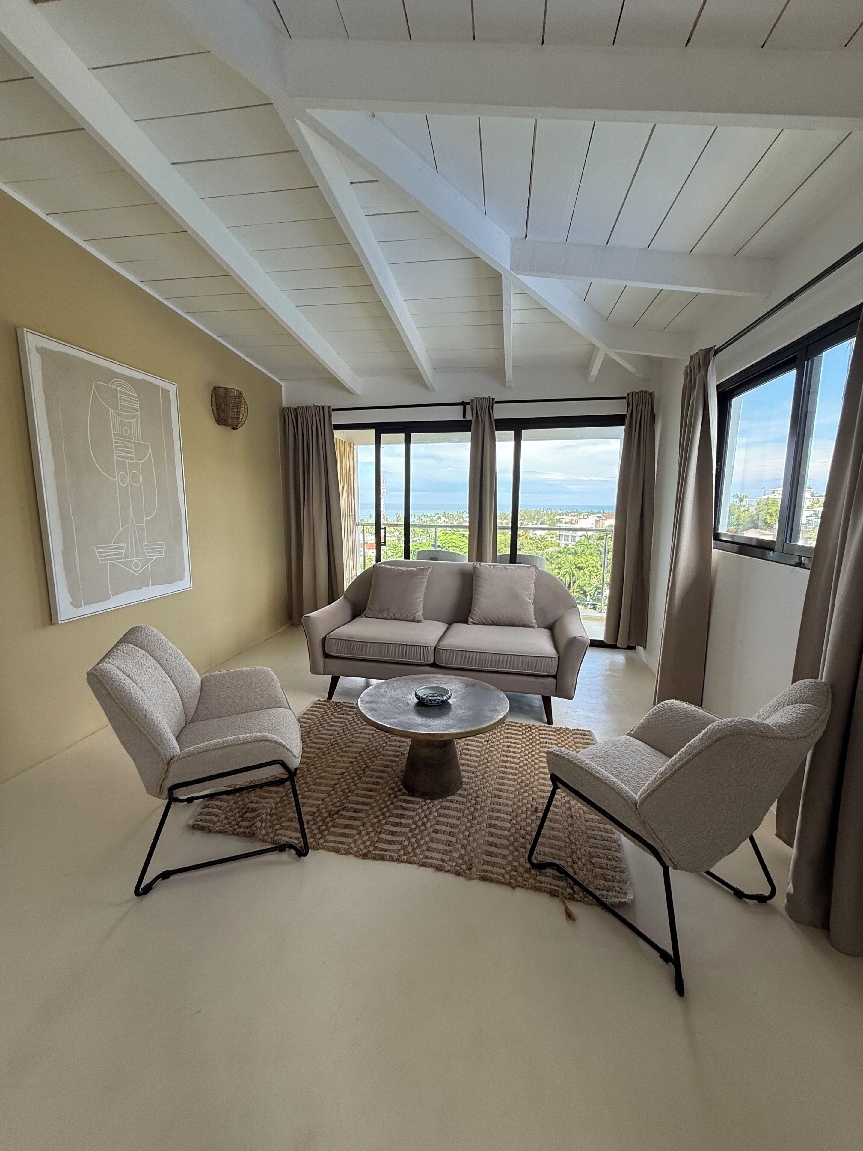 Un salon moderne comprenant un canapé, deux fauteuils, une table basse et une vue sur l’extérieur.