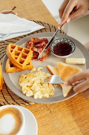 Un plato de desayuno con waffles, tocino, huevos revueltos, tostadas y una taza de café.