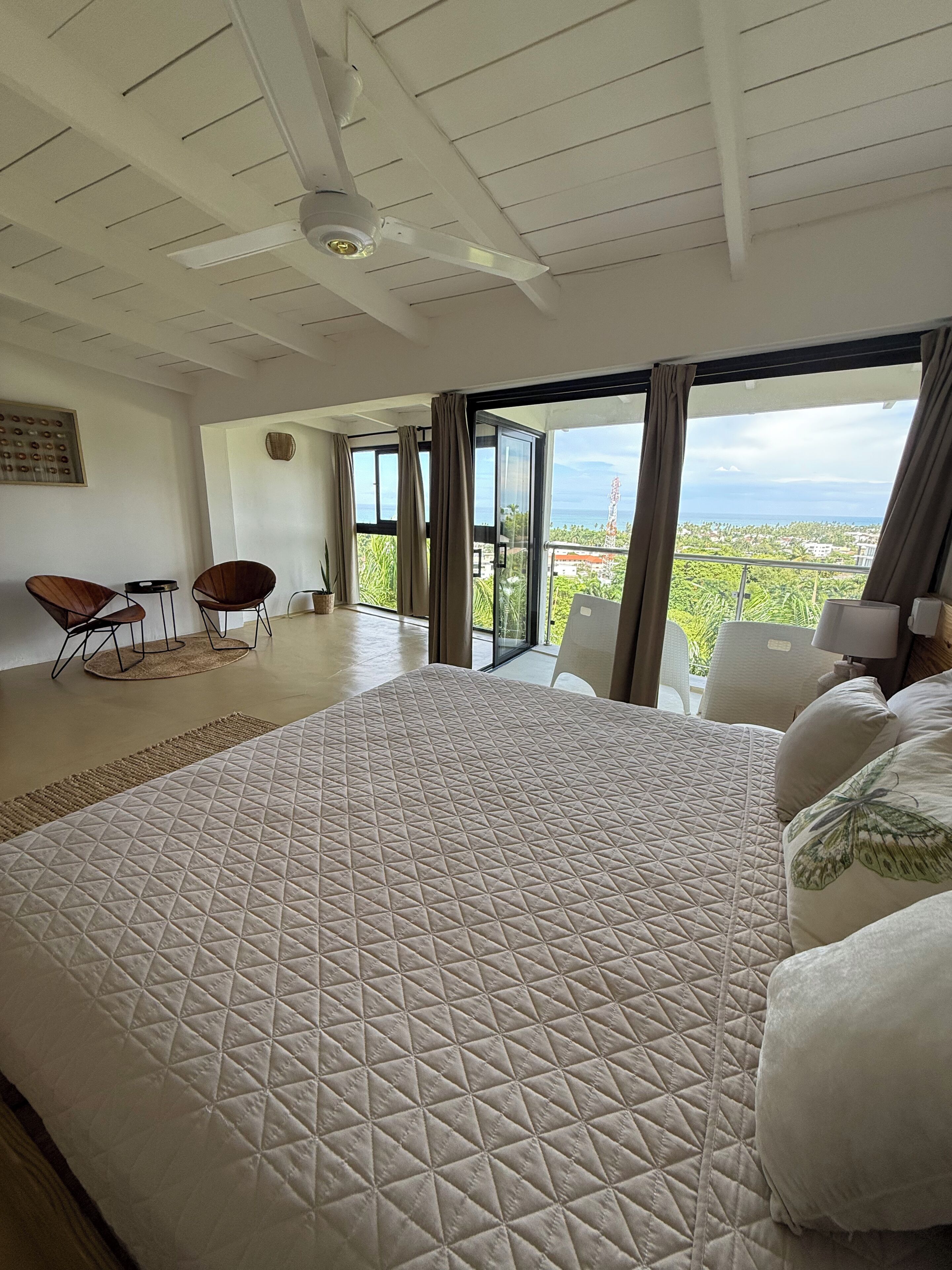 A spacious bedroom with a large bed, a ceiling fan, and a view of the ocean.